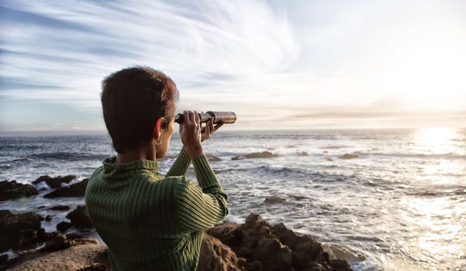 person with spyglass looks at ocean horizon